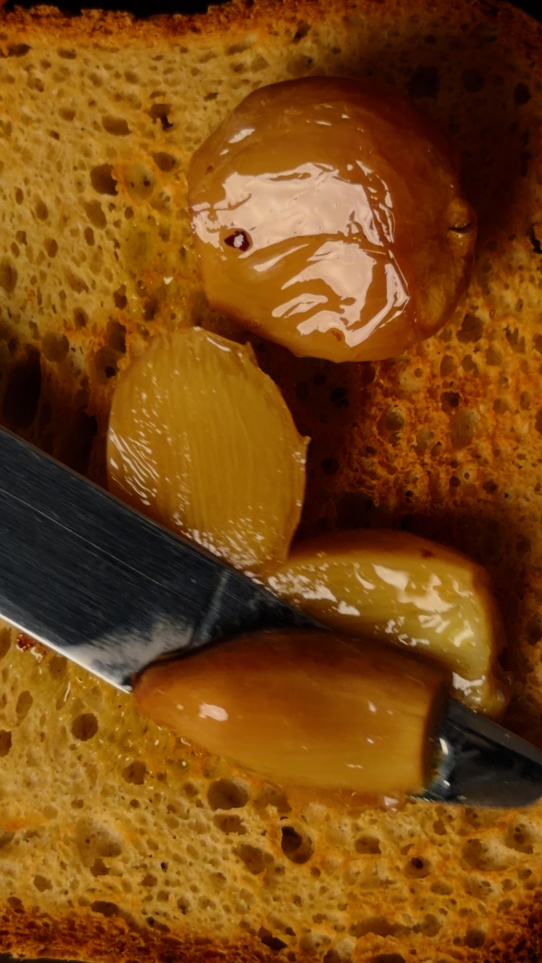 Golden confit garlic cloves glistening on toast, spread with a knife