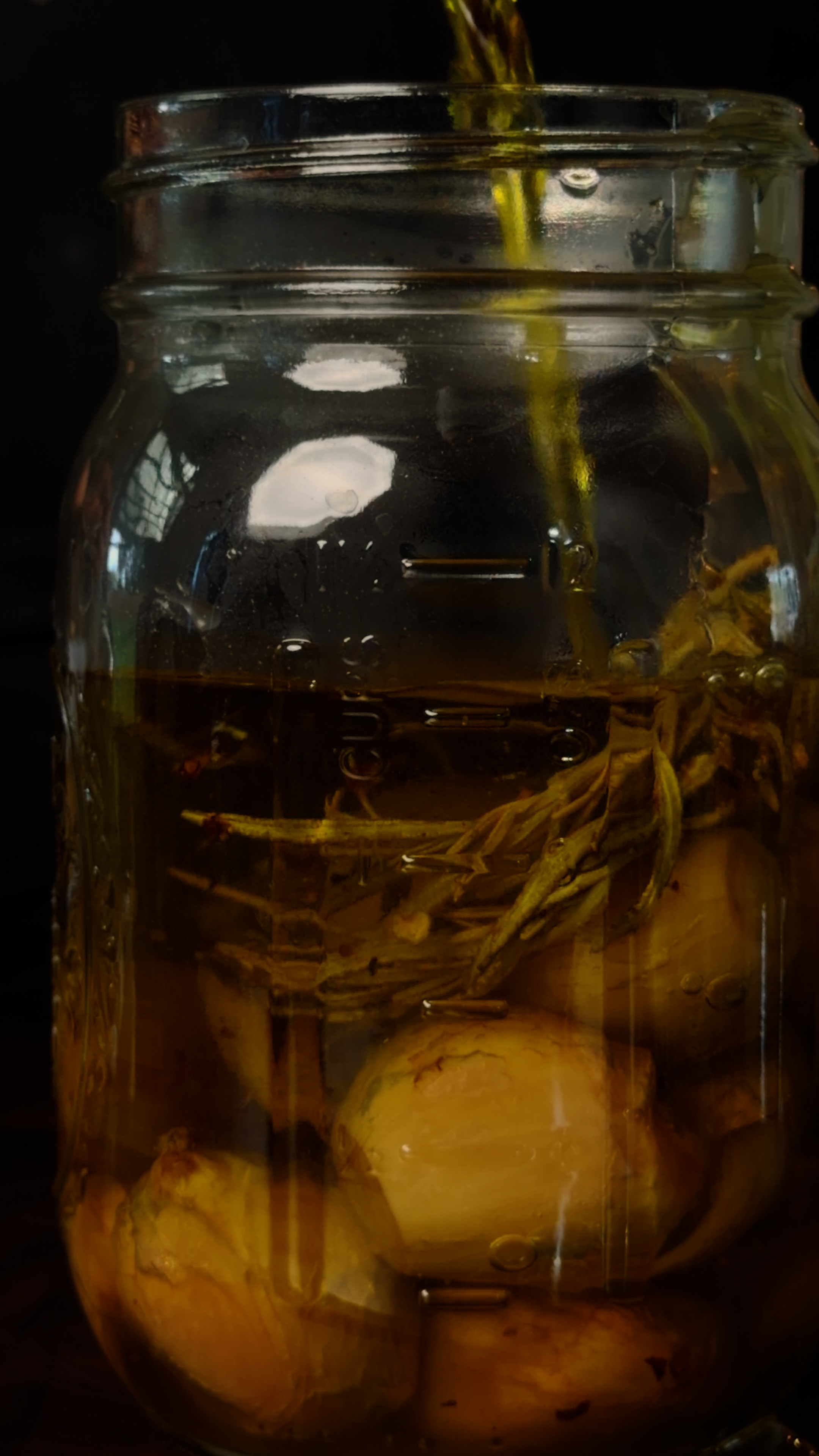 Garlic confit oil with rosemary being poured into a mason jar