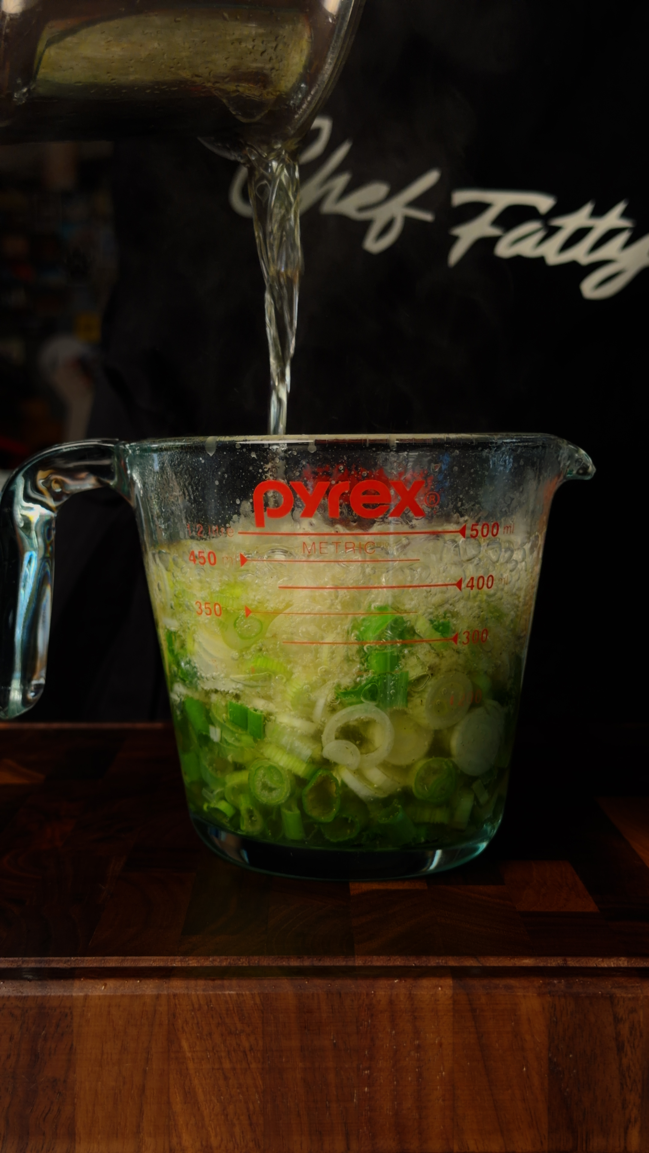 Hot oil being poured over chopped scallions and ginger in a Pyrex measuring cup