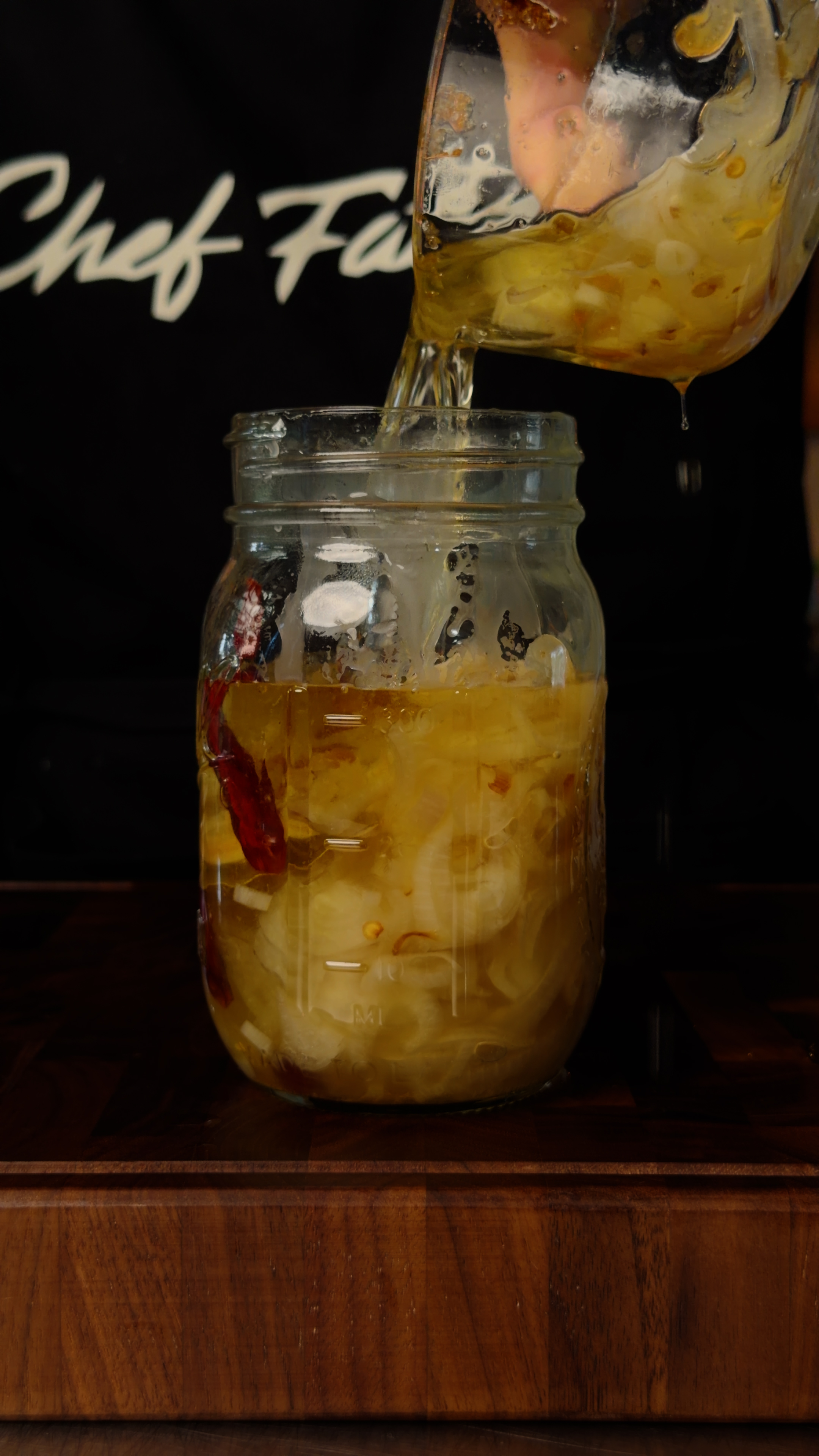 Raw shallots and arbol chiles with oil being poured into a glass bowl
