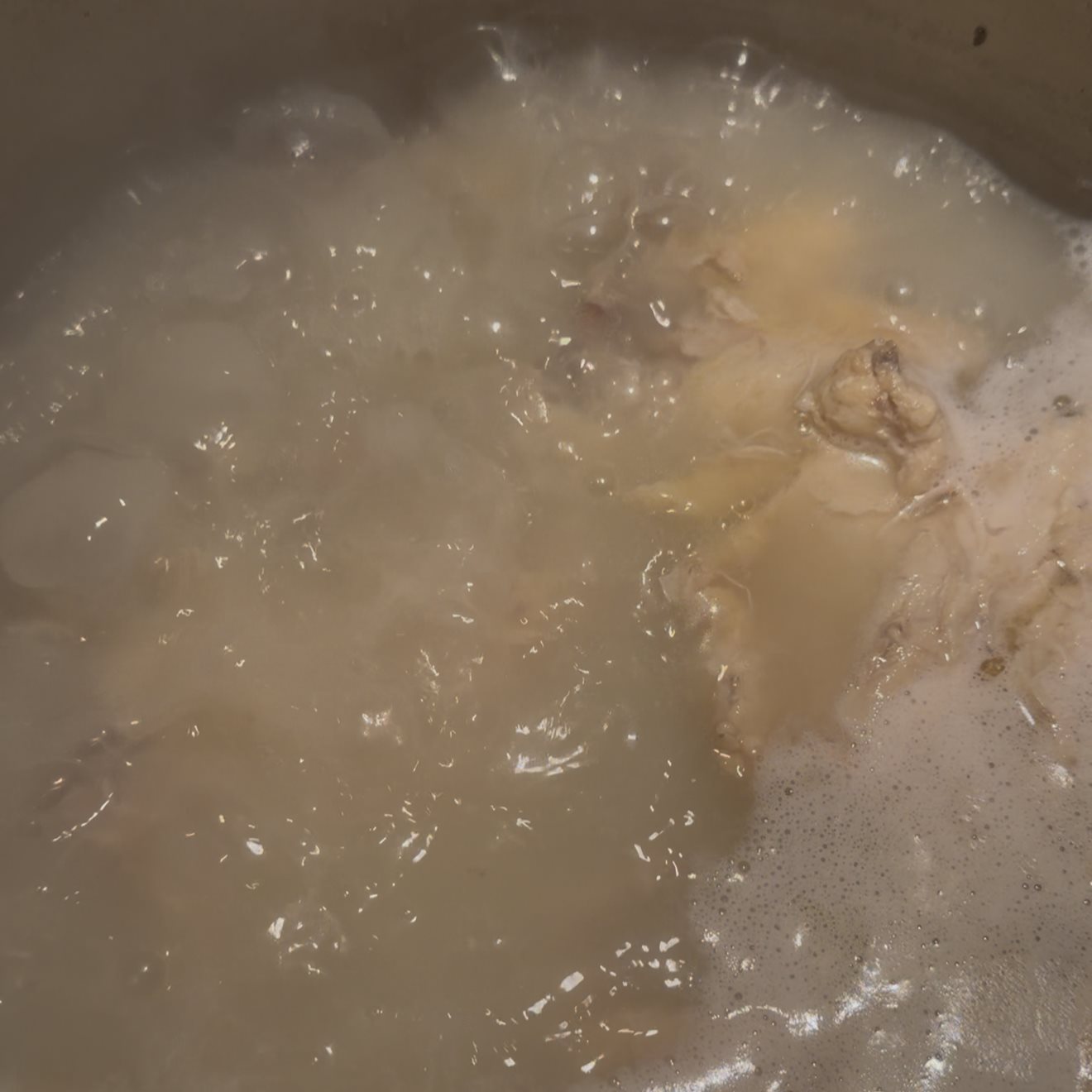 Chicken stock simmering in a pot with grey foam rising to the surface