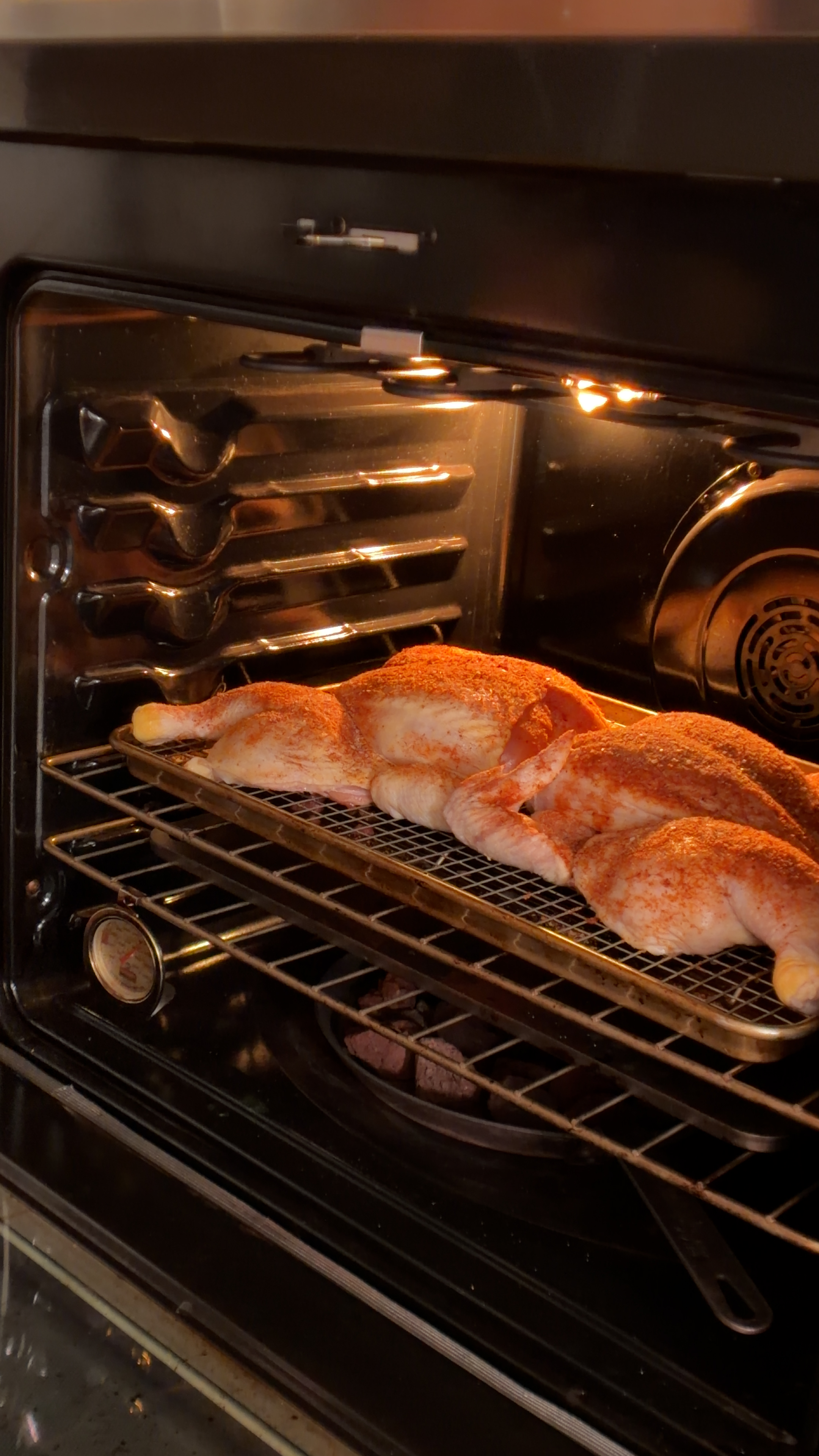 Seasoned spatchcocked chicken on a wire rack over a baking sheet inside a preheated oven