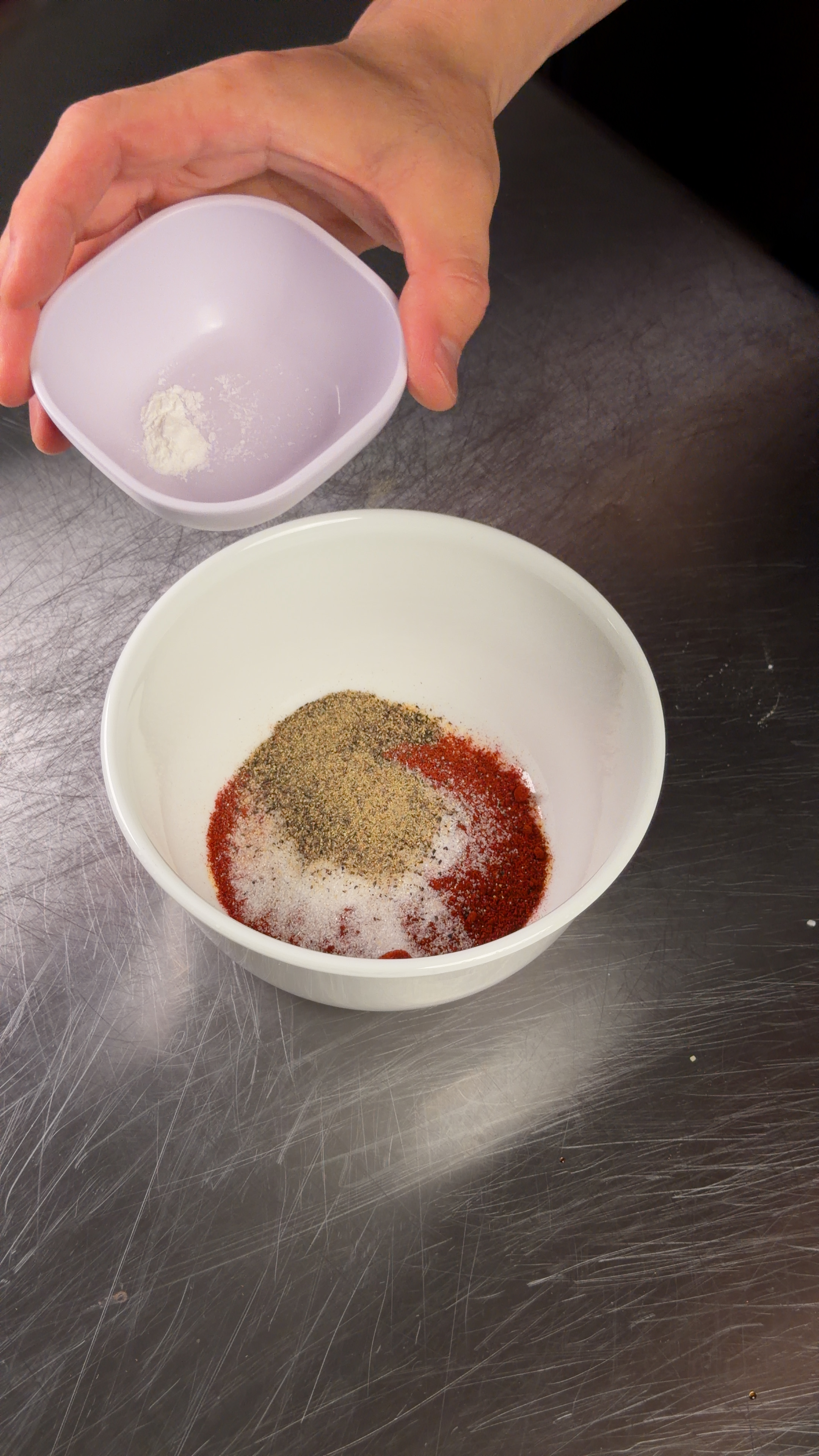 Spice rub with paprika, salt, and pepper in a white bowl with baking powder being added
