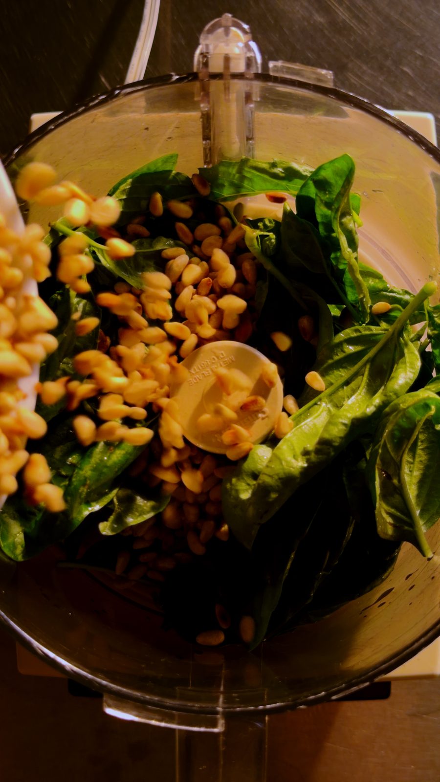 Fresh basil and pine nuts in a food processor bowl, the start of pesto