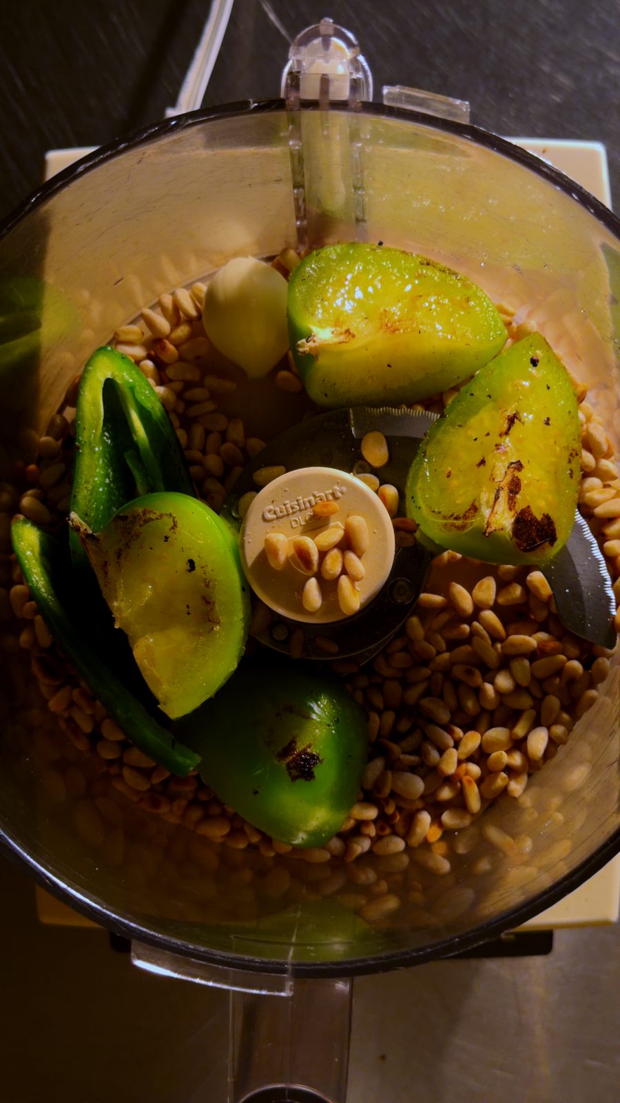 Toasted pepitas, charred tomatillo, garlic, and chili in a food processor bowl