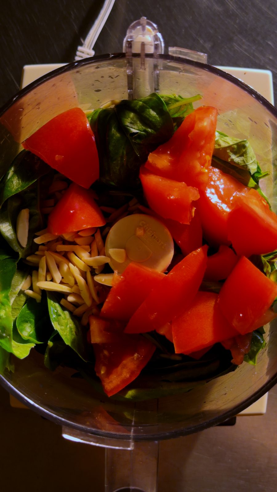 Basil, ripe tomatoes, and slivered almonds in a food processor bowl