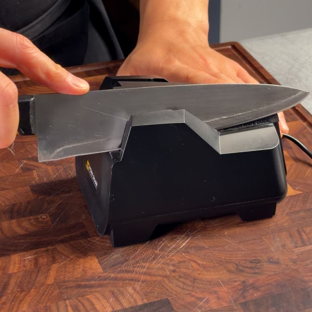 Hands running a chef knife through a black electric knife sharpener