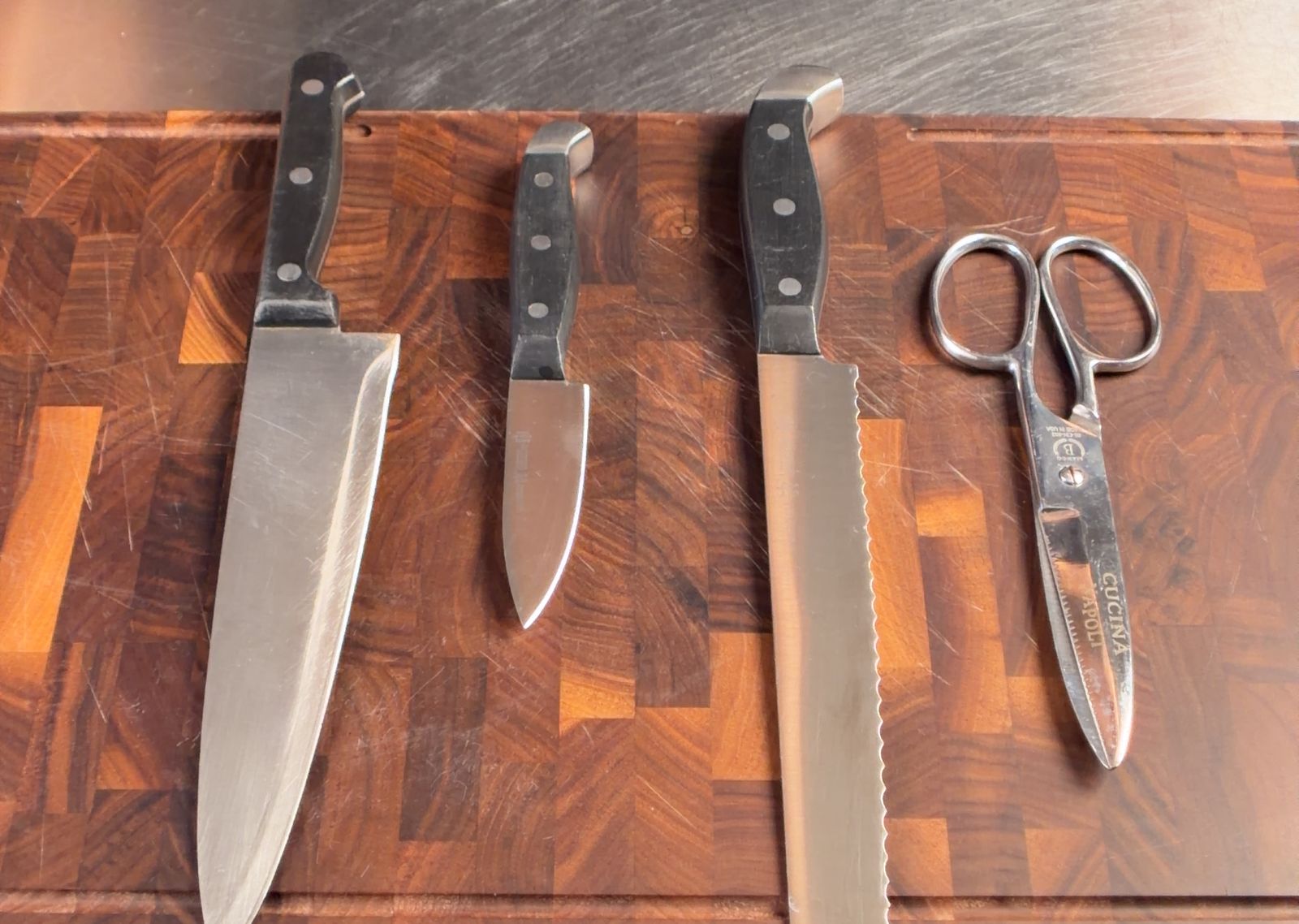 A chef's knife, paring knife, bread knife, and kitchen shears on a wood cutting board