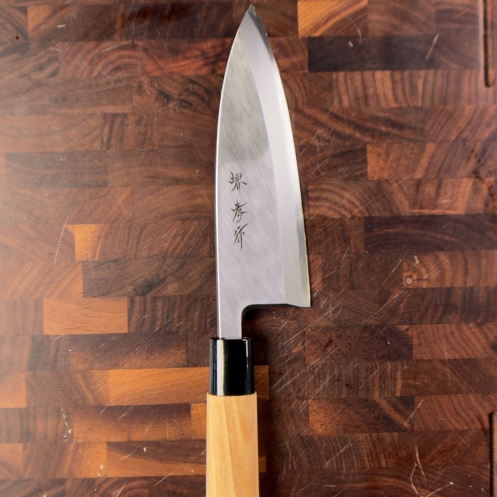 A single-bevel Japanese knife with kanji on the blade and a light wood handle