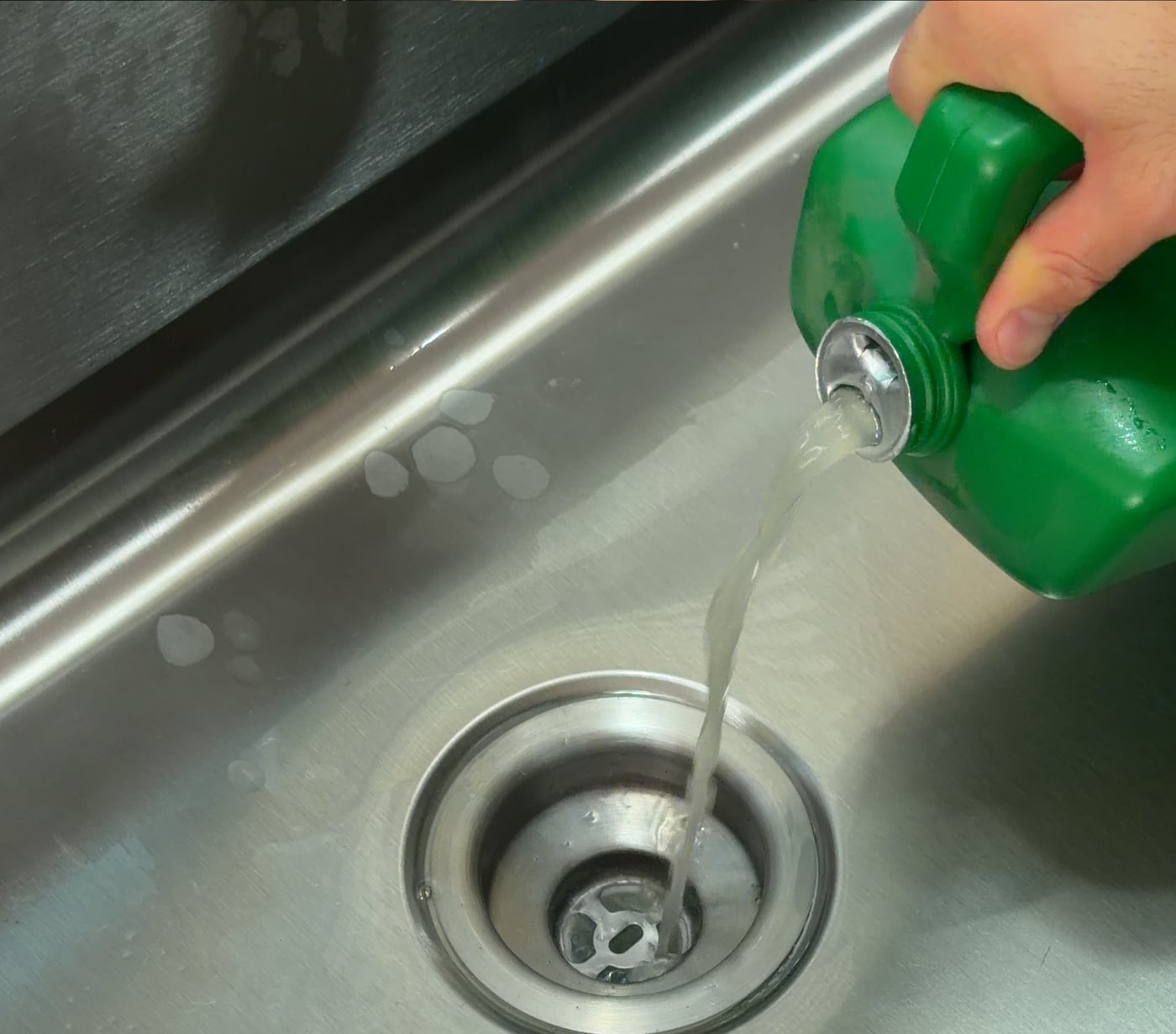 Pouring Green Gobbler enzyme drain cleaner into a kitchen drain