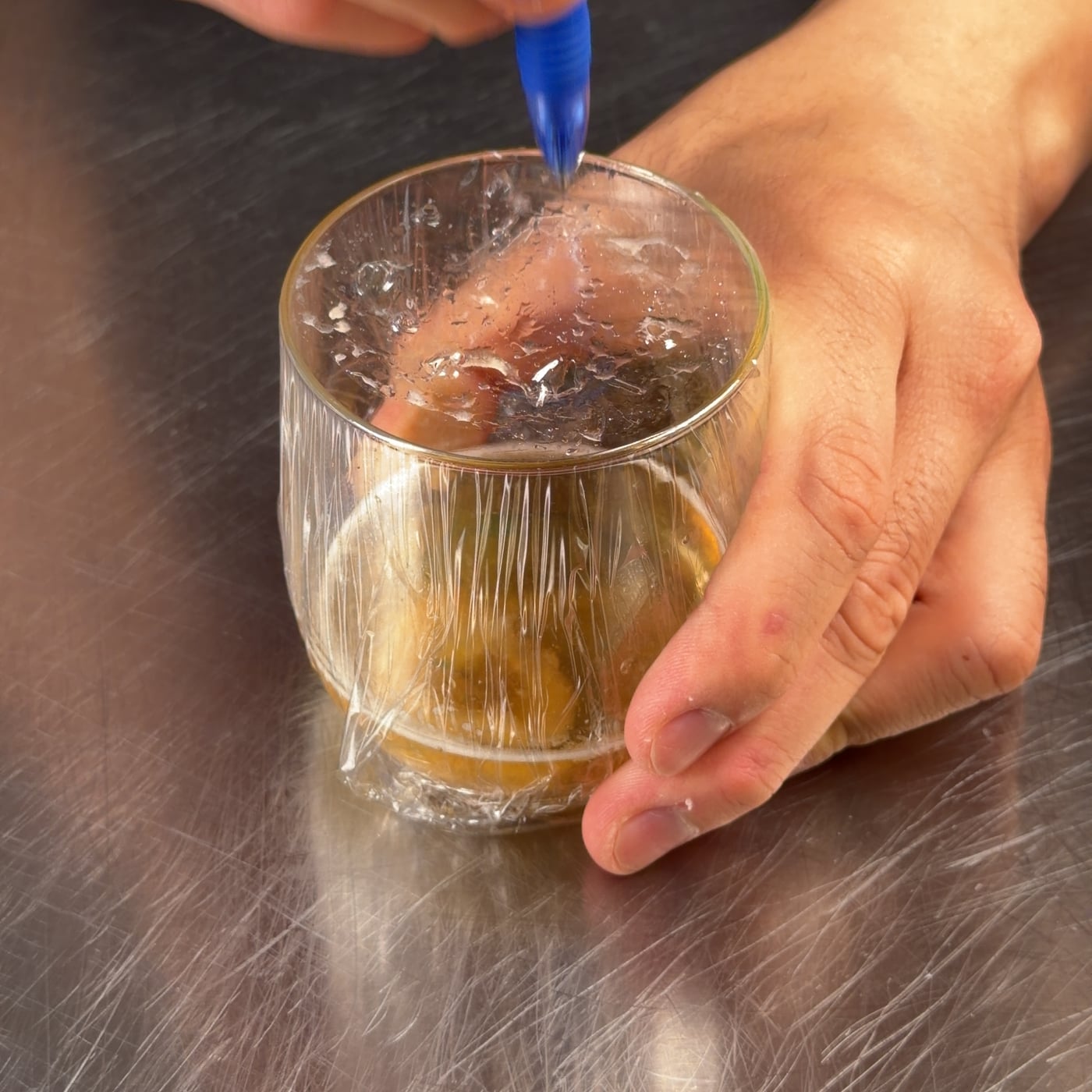 Hand poking holes in plastic wrap covering a glass with apple cider vinegar trap inside