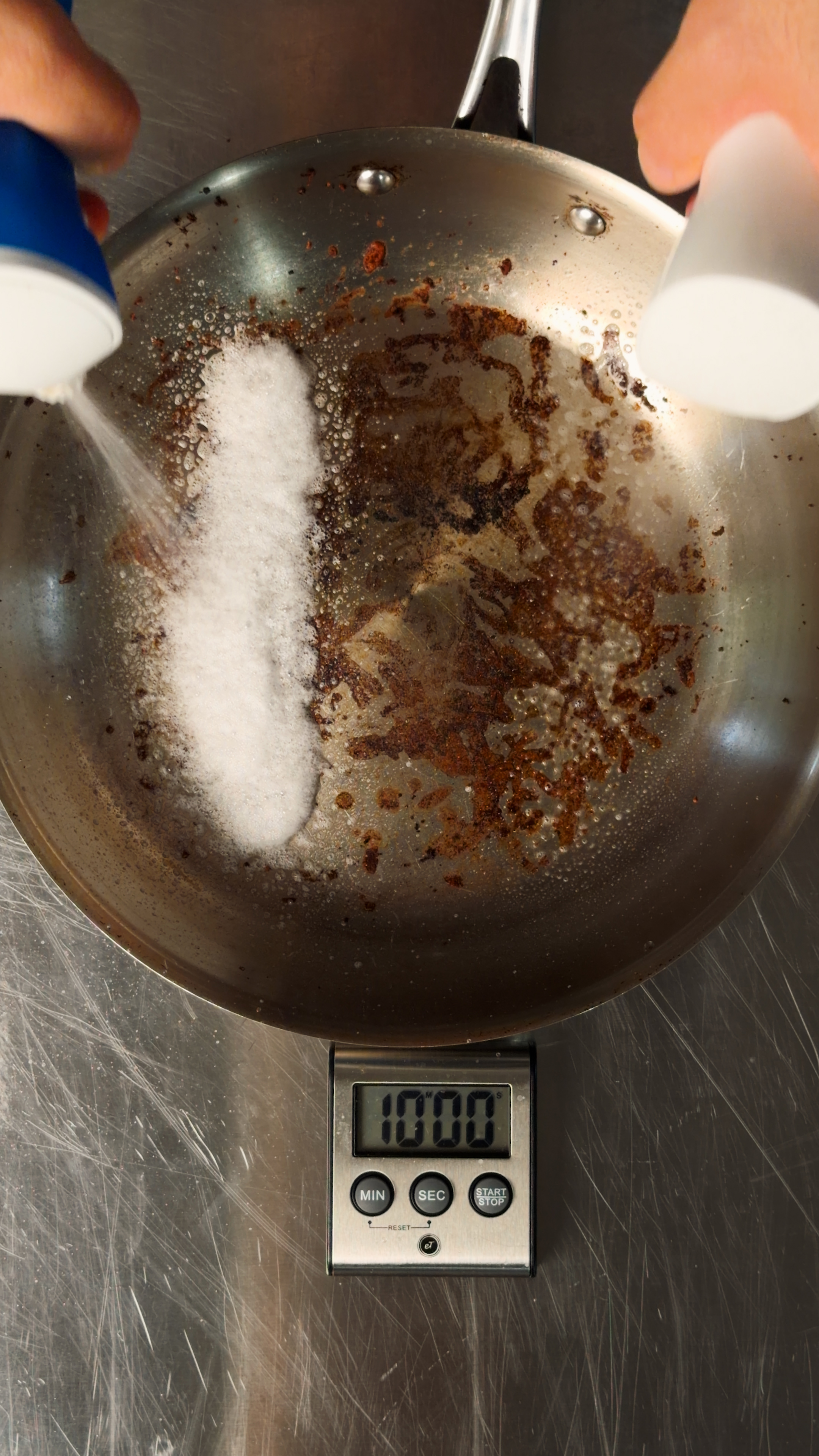 Stainless pan with cooked-on residue, dish spray applied to both halves, a timer reading 10:00 in front of it