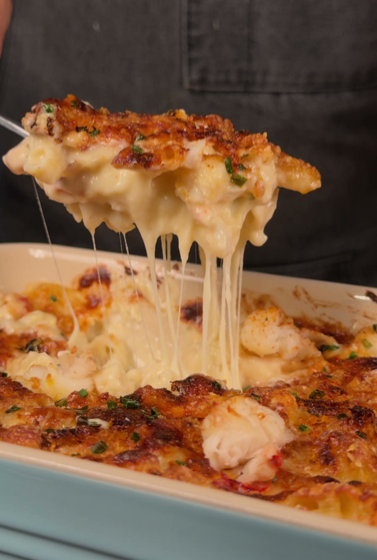 A scoop of lobster mac and cheese lifted from the dish with a long stretchy cheese pull.