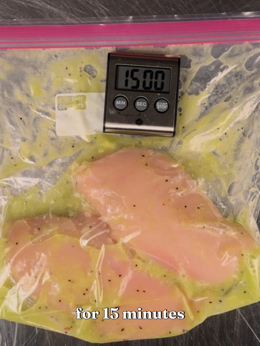 Chicken breasts in a bag of green kiwi marinade next to a timer showing 15:00
