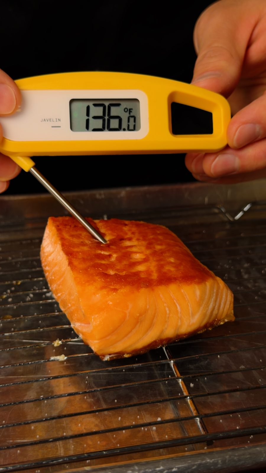 An instant-read thermometer probing a seared salmon fillet on a rack and reading 136 degrees Fahrenheit