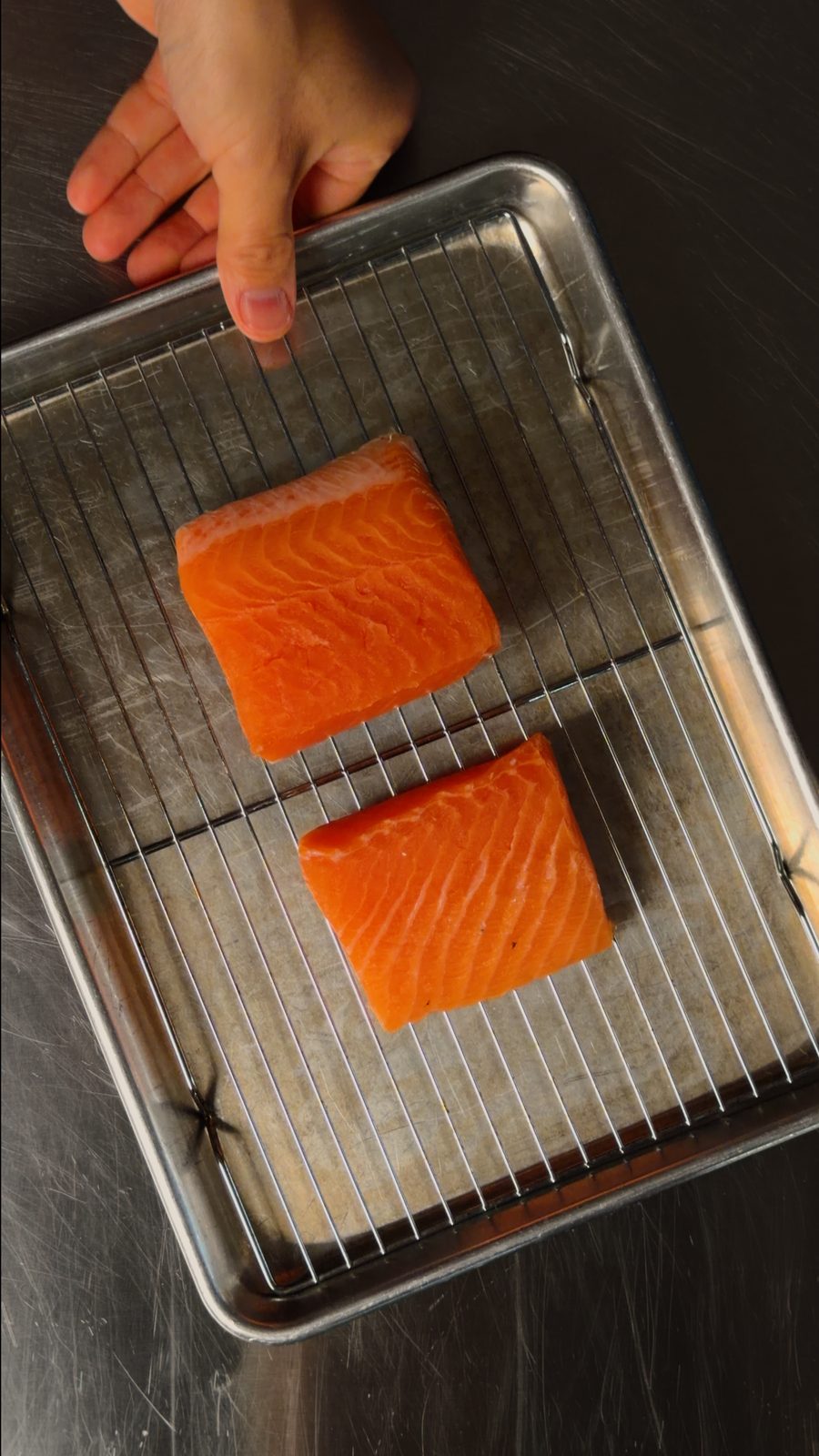 Two raw skin-on salmon fillets sitting on a wire rack set inside a sheet pan