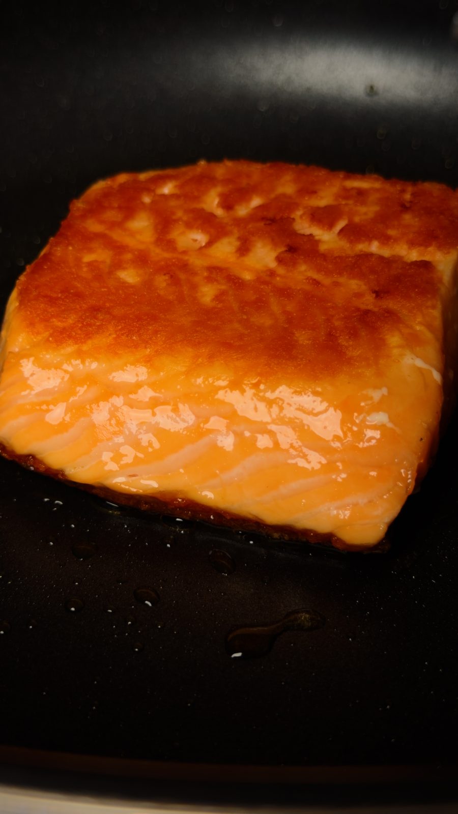 A salmon fillet seared to a deep golden brown crust resting in a nonstick pan
