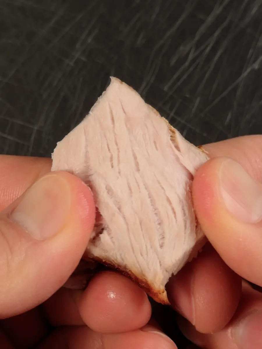 Fingers pulling apart a piece of overcooked pork, showing pale, dry, fibrous strands