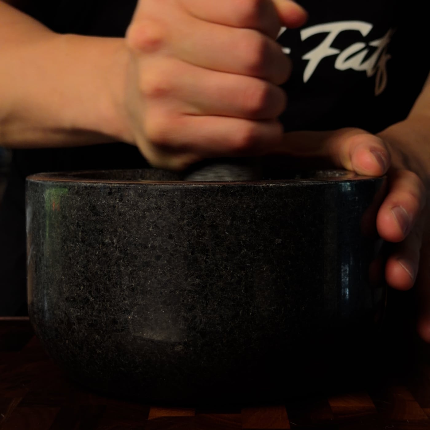 Roasted garlic cloves being mashed into a smooth paste in a stone mortar with a wooden pestle