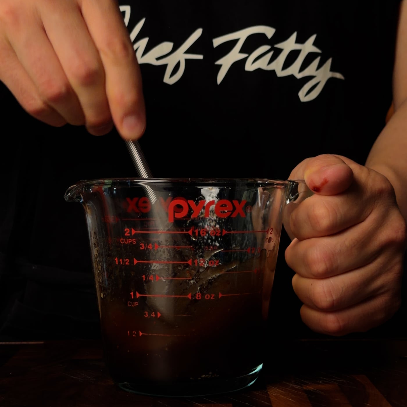 Pyrex measuring cup with dark balsamic strawberry vinaigrette being whisked, Chef Fatty apron in background