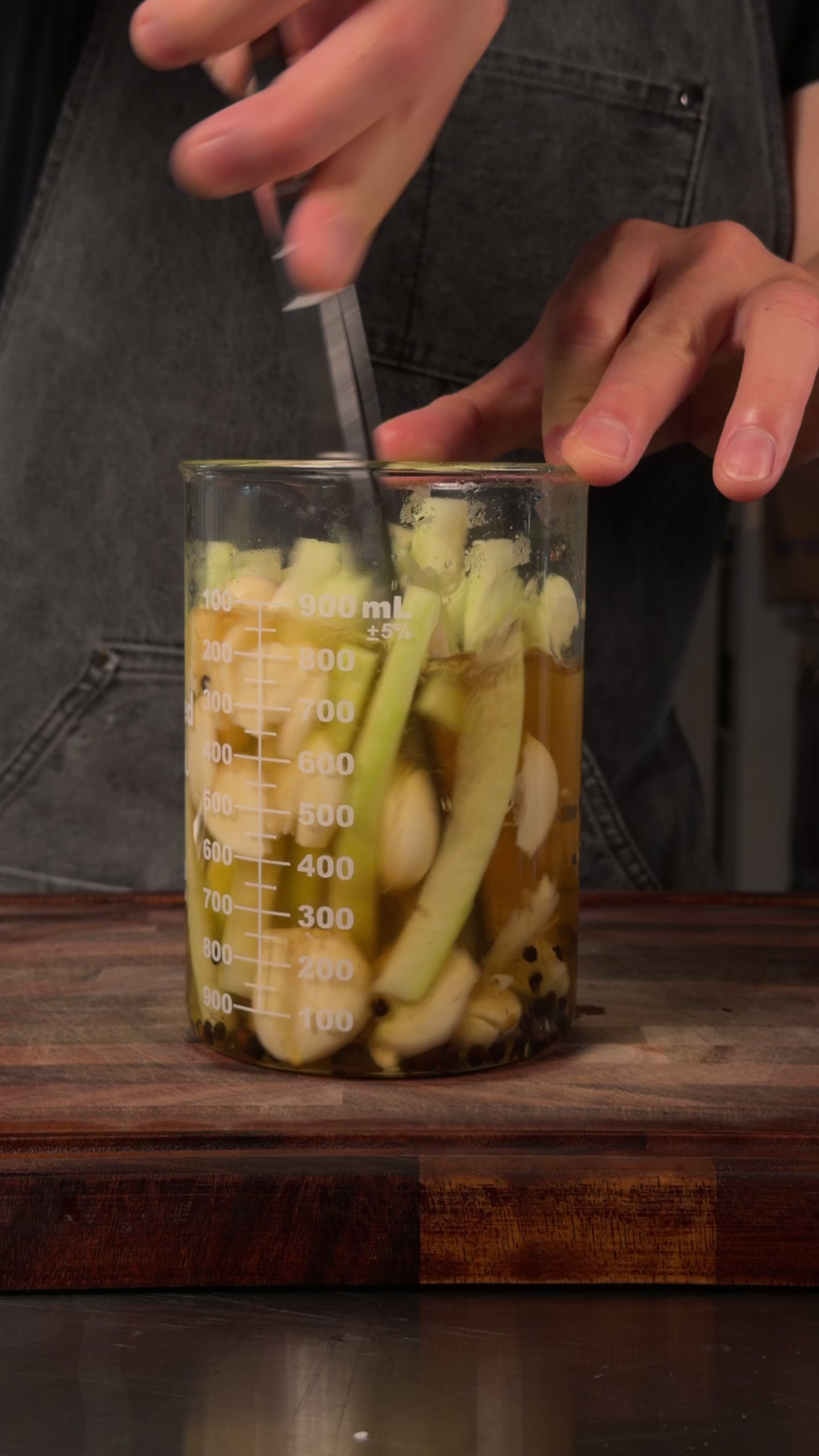 A jar of watermelon rind batons brining with garlic and black peppercorns.