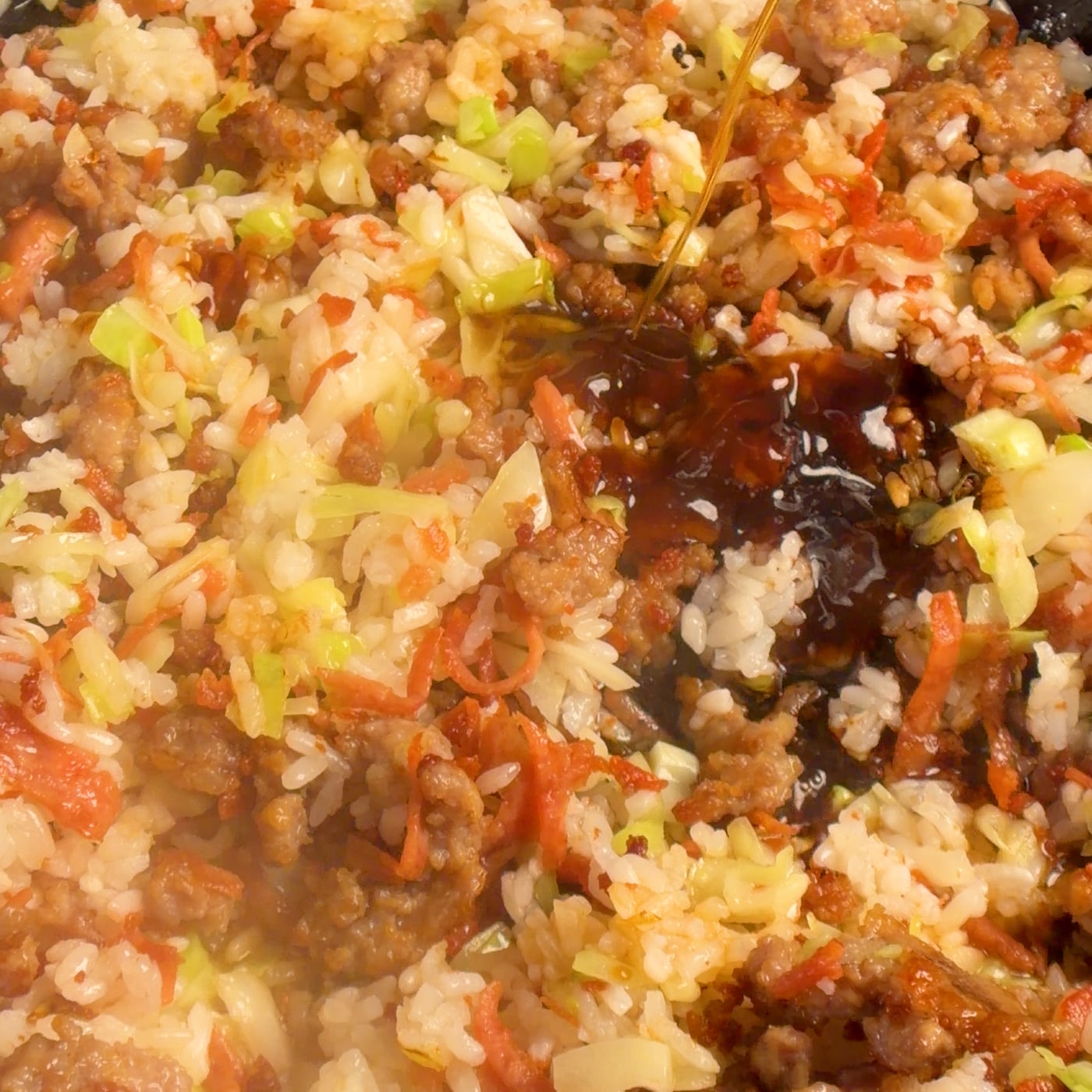Soy and oyster sauce being poured around the edge of a hot enameled cast iron pan with fried rice