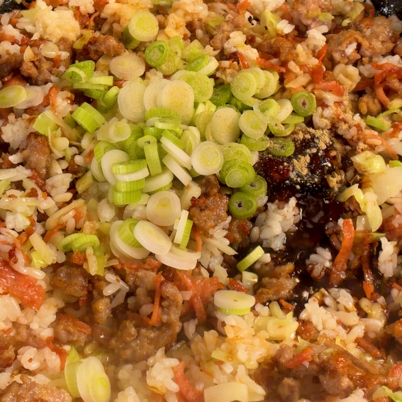 Sliced raw green onions added to crispy pork fried rice in a thin enameled cast iron pan