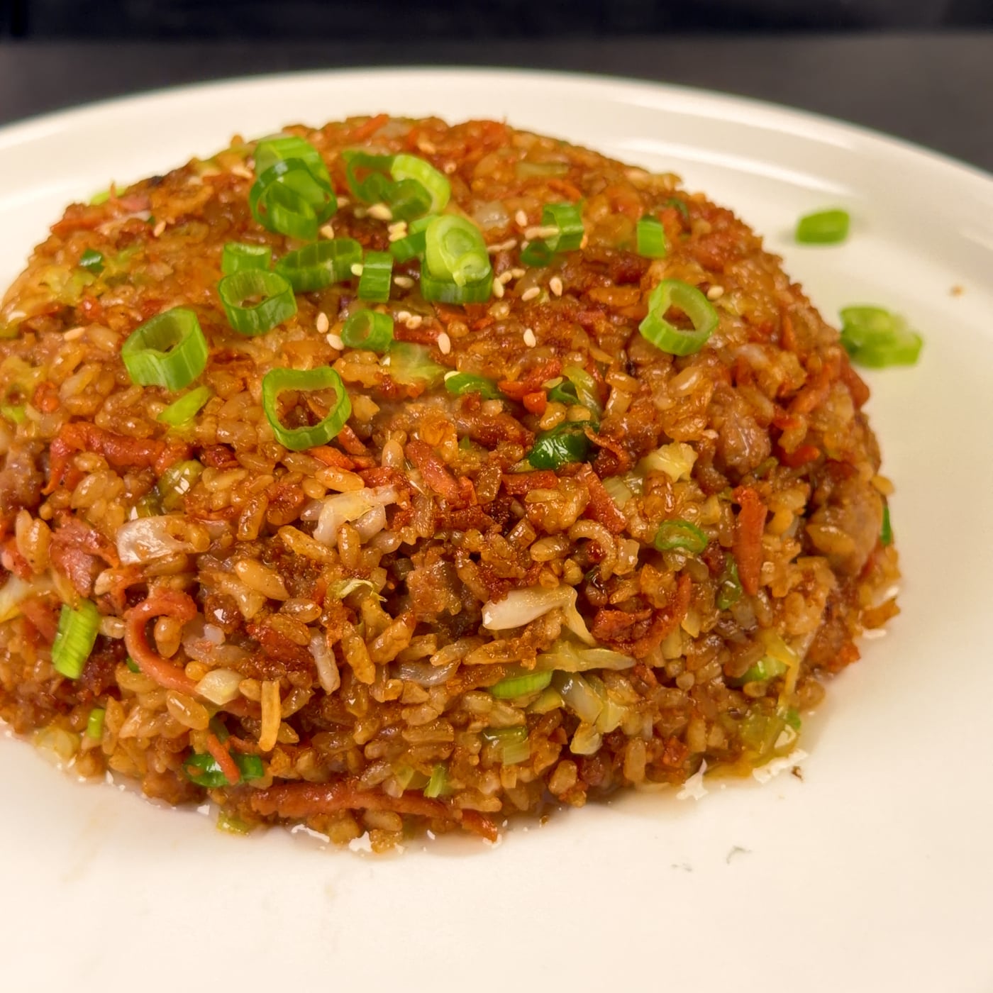 Plated crispy pork fried rice molded into a dome with sesame seeds and sliced green onions on top