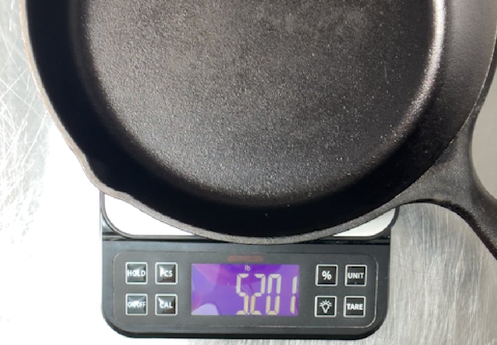 Traditional 10-inch cast iron skillet on a digital kitchen scale reading 5201 grams