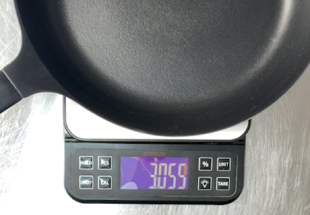 Thin enameled cast iron pan on a digital kitchen scale reading 3059 grams