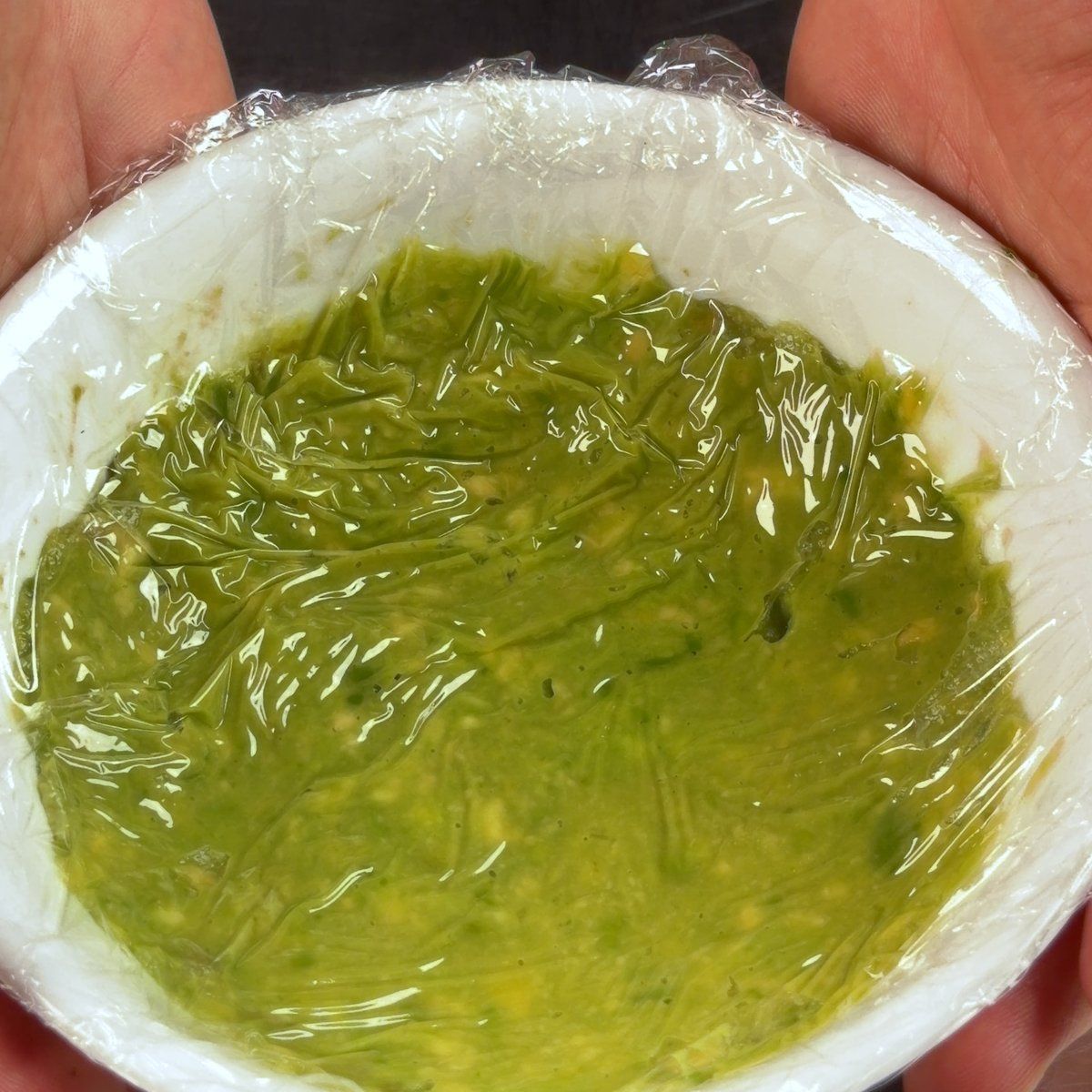 Guacamole in a bowl with plastic wrap pressed directly against the surface to limit oxygen contact