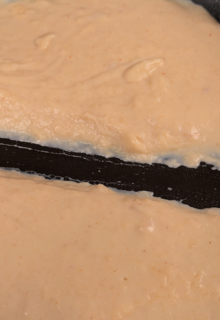 A very thick white sauce holding an open line drawn through it with a spatula, the pan visible in the gap