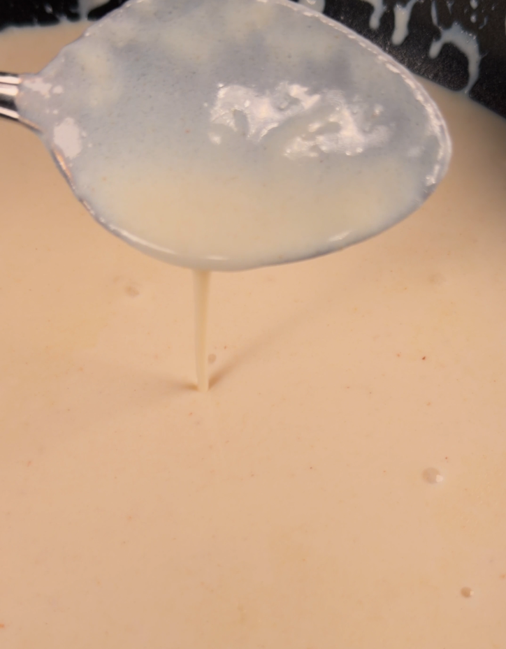 A thin pourable white sauce running off a spoon in a delicate stream into the pan below