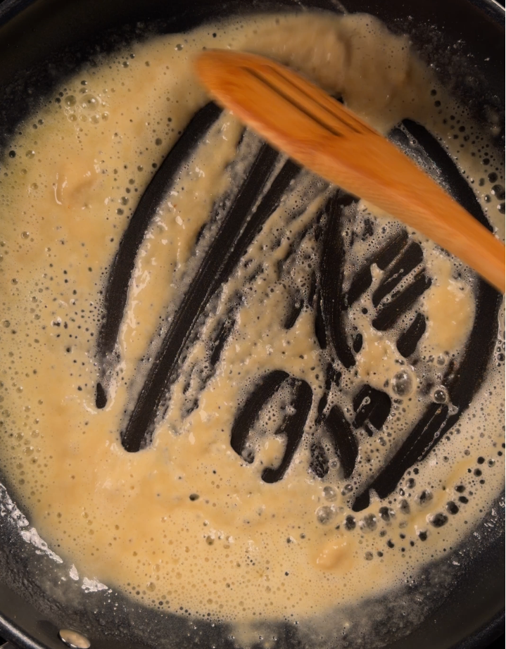 Butter and flour cooked together into a pale bubbling roux in a dark pan, a wooden spoon dragging a clean trail through it