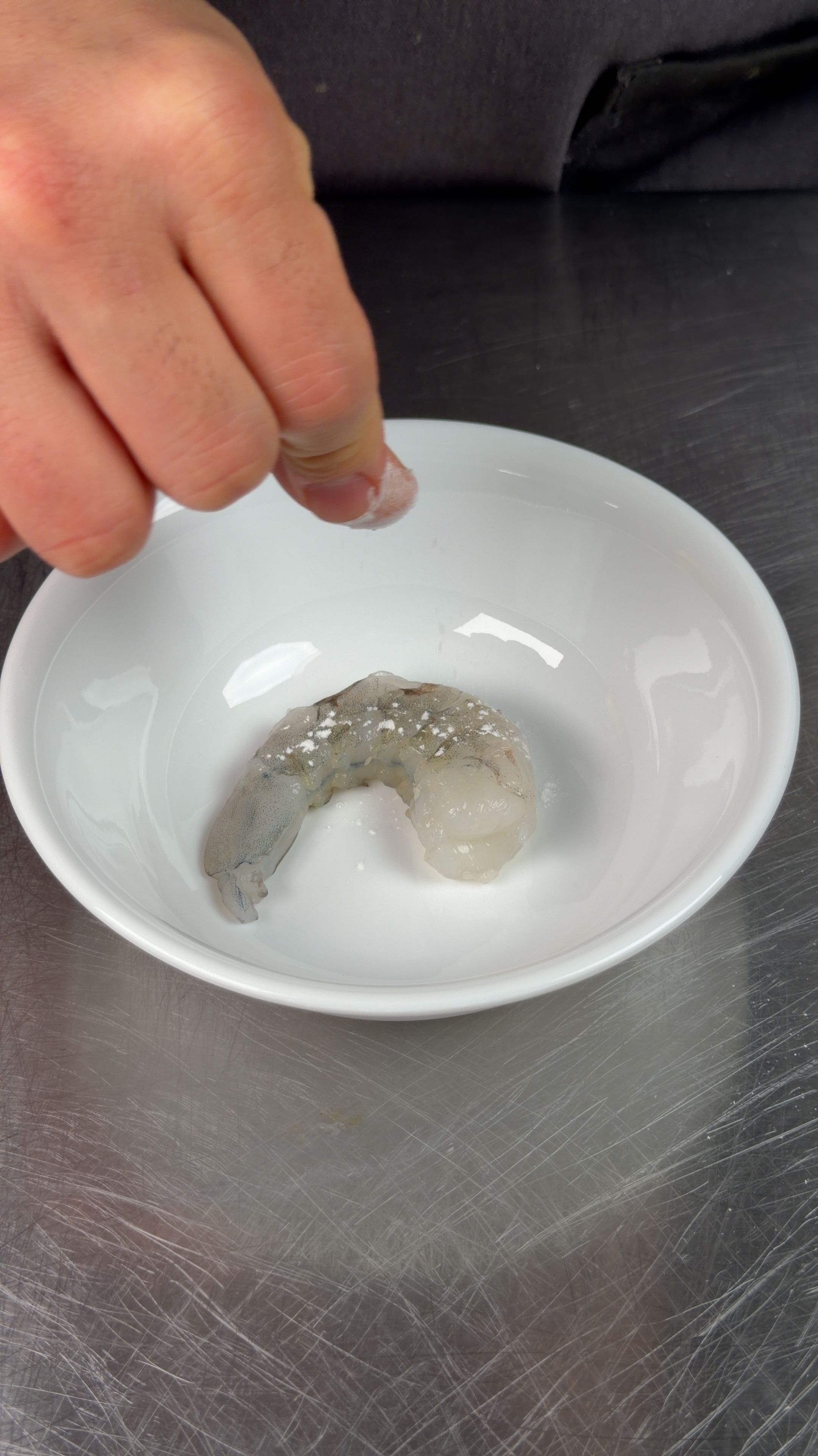 Raw shrimp in white bowl being dusted with baking soda