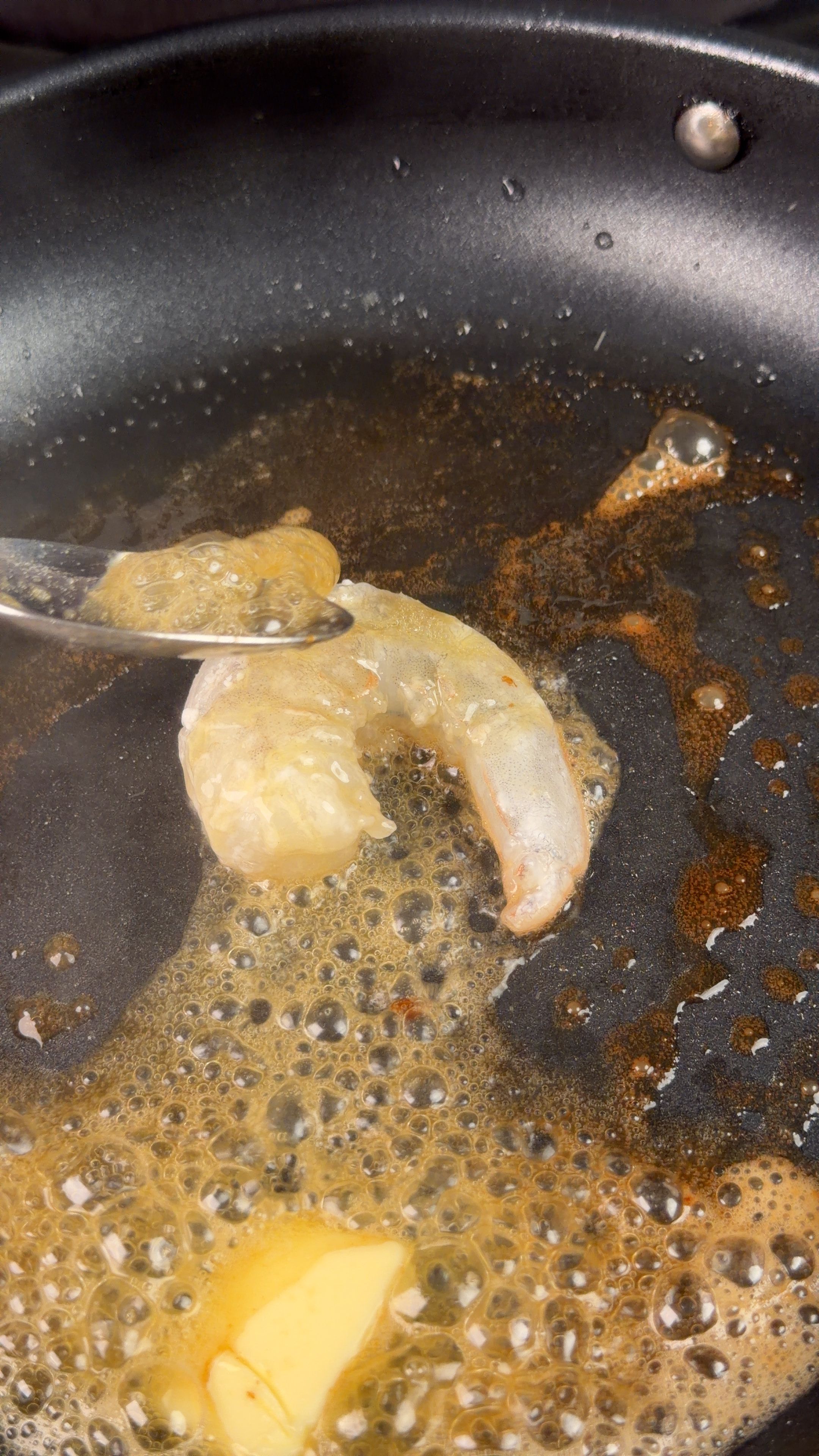 Shrimp being butter basted in a sizzling pan